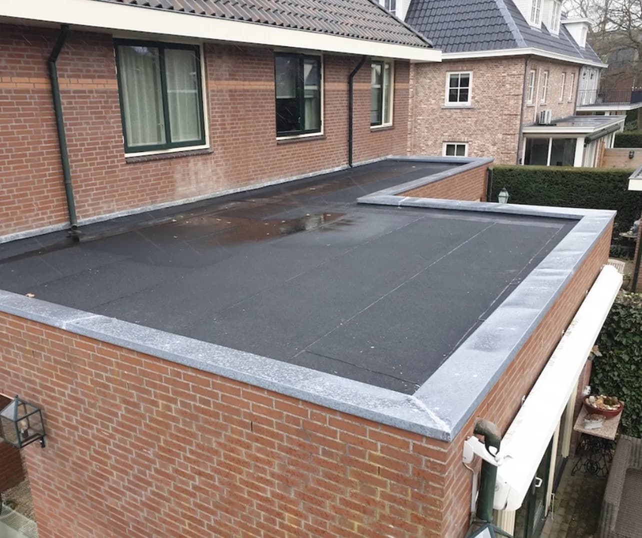 Zwart bitumen dak op een bakstenen aanbouw met nieuwe daktrim en zinken hemelwaterafvoer